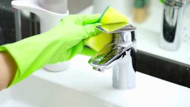 Housewife in rubber gloves washing faucet in bathroom with sponge and detergent closeup 4k movie