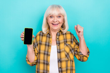 Photo of excited aged woman rejoice luck triumph hooray fists hand hold mobile isolated over teal...