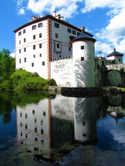 Fototapeta na wymiar Beautiful medieval Sneznik castle in Notranjska, Slovenia with a reflection in the water and white clouds in blue sky behind