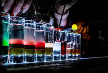 woman bartender hand making collection of colorful shots. Set of cocktails at the bar counter