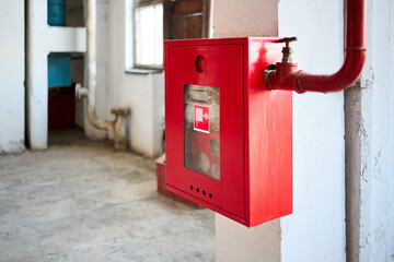 Fire hose in red box. Pipe roll for fire emergency in red metal cabinet on grey whitewashed wall as part of fire fighting system of industrial production plant with copyspace.