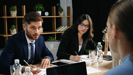 young man talking to blurred colleague near businesswoman writing in notebook