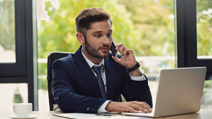 young businessman looking at laptop during conversation on mobile phone