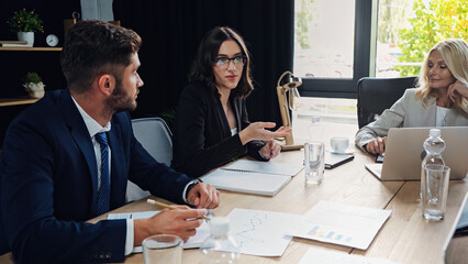 businesswoman in eyeglasses pointing with hand while talking to colleagues during meeting