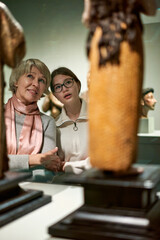 Teenage girl and mature woman observing exhibition in historical museum