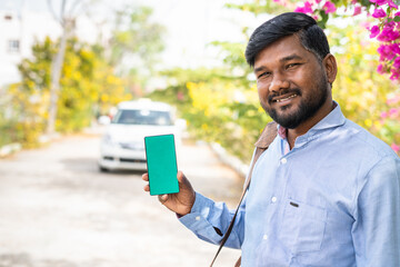 Smiling young passanger showing green screen mobile phone by looking at camera - concept of online cab or taxi booking service, app advertising and promotional offers.