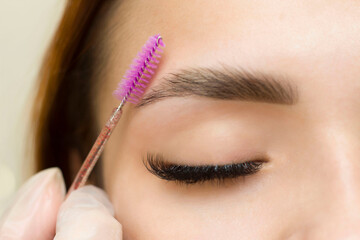 The makeup artist combs his eyebrows with a brush. Eyebrow styling. Permanent makeup. Coloring with...