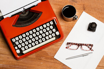 Máquina de escribir antigua, junto a una taza de café, hojas, gafas y boligrafo sobre un fondo de...
