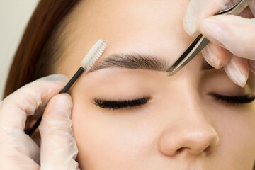The makeup artist combs her eyebrows with a brush and tweezers. Eyebrow styling. Permanent makeup....