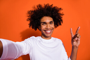 Photo of cheerful positive guy wear white shirt half recording self video v-sign isolated orange color background