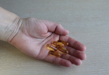 In a woman's hand are vitamins in yellow capsules.