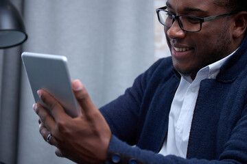 Close-up of a smiling African entrepreneur with glasses using a digital tablet. A black man in a white shirt and jacket uses an information portable device