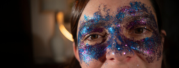 Close up of a beautiful woman's eyes made up with blue and purple particles forming a mask against a dark out of focus background