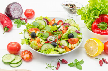 Healthy fresh vegetable salad with tomatoes, cucumbers and bell peppers in a plate on a white wooden background