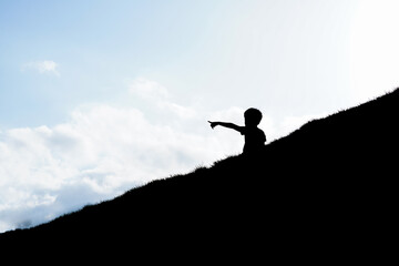 Silhouette of a child on the hill with sky background.