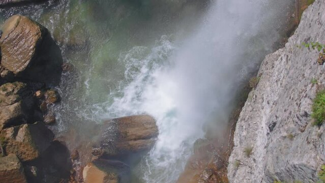 Waterfall falling down into the river and stone boulders. Slow motion, high angle view. 