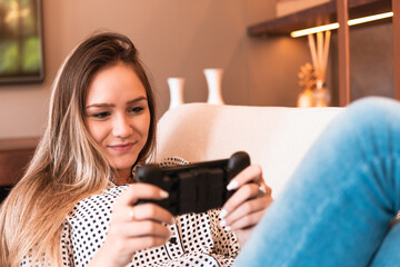happy woman using mobile phone for game and sitting in armchair in living room