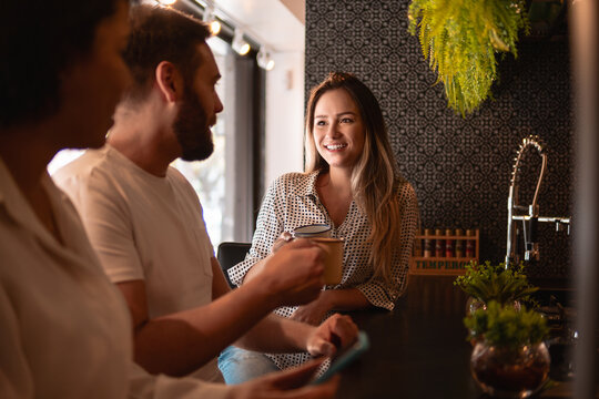 Happy Woman Talking To Friends And Drinking Coffee In Kitchen Counter