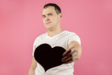 A young caucasian man with a big black heart shows his anger, disgust, sadness about the onset of...