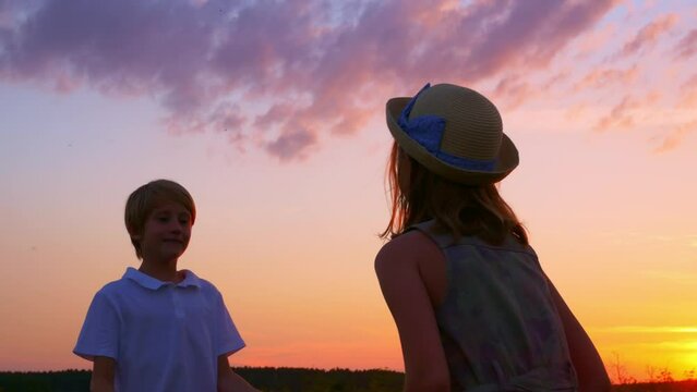 Brother and sister play ball, throw the ball into each other's hands. Teenagers girl and boy have fun playing in the backyard in the rays of the setting sun. Children's dreams