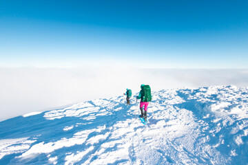 Naklejka na ściany i meble Two women with backpacks walk in snowshoes in winter trekking