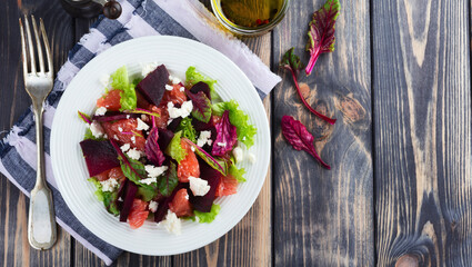 Salad of beets, lettuce, beetroot leaves, grapefruit and feta cheese on the old wooden background. Selective focus. - obrazy, fototapety, plakaty