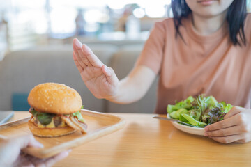 Young woman pushing away plate  hamburger from waitress for good health. Weight loss concept. diet concept. No Food waste concept. 