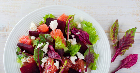 Salad of beets, lettuce, beetroot leaves, grapefruit and feta cheese on the old wooden background. Selective focus.