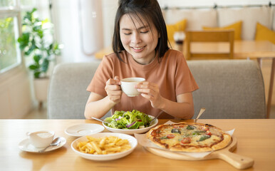 Obraz na płótnie Canvas A woman drinking coffee with feeling happy and enjoy to eat food in the restaurant in leisure time. dine in the restaurant, eating delicious served hot pizza and salad. Eating concept. Italian food.