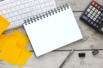 Blank open notepad on wood table, flat lay photo of office desk with calculator keyboard and yellow sticky notes