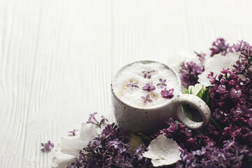 Obraz na płótnie Canvas Delicious coffee with lilac petals, rose and lilac branch on rustic white wooden background. Hello spring. Space for text. Happy mothers day. Good morning still life