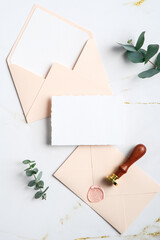 Wedding stationery set. Top view blank paper card, envelopes, wax seal stamp, eucalyptus branches on white marble table. Top view. Flat lay.