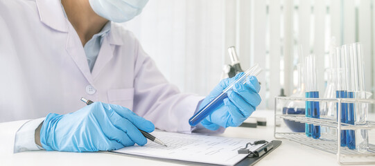Scientist looking at test tube with clear solution in pharmaceutical research laboratory.