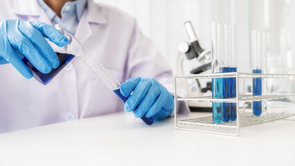 Fototapeta premium Scientist pouring a beaker with clear solution into a test tube in pharmaceutical research laboratory. Innovation Concept.