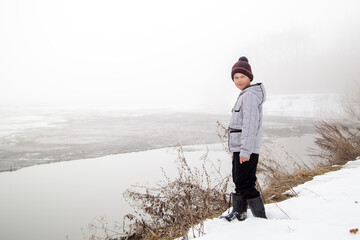 a boy stands on the bank of a river on a spring day before the ice breaks