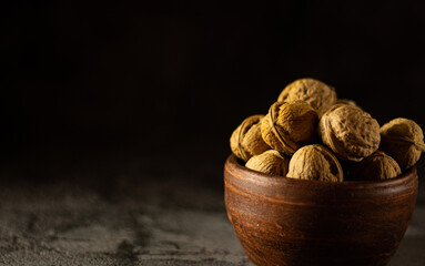 Whole walnuts in vintage bowl on black background
