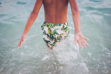 Close up of young boy's back walking into the ocean.