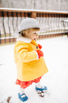 Baby girl walking in snow, wearing hat and yellow coat