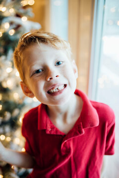 Young boy smiling next to Christmas tree and window