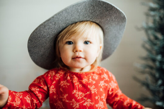Toddler girl looking at camera, wearing gray hat red dress