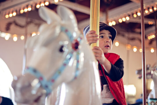 Young boy wearing a red vest on a horse at a carrousel.