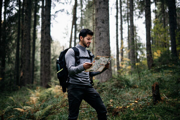 Happy man with backpack reading the map in the forest