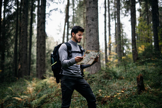 Happy man with backpack reading the map in the forest