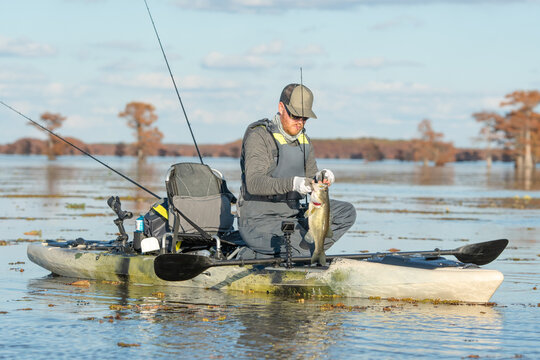 man catching largemouth bass from kayak