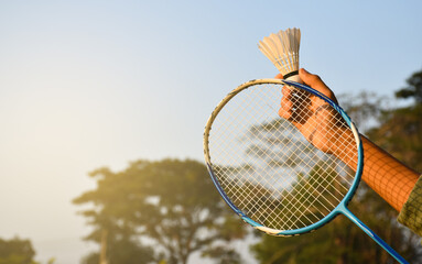 Badminton racket and new badminton shuttlecock holding in hand of player, blurred outdoor and sunset background. concept for badminton lovers around the world.