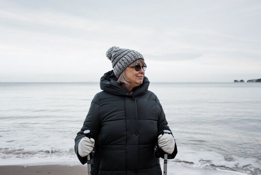 woman in her 70's walking with sticks along the beach in winter