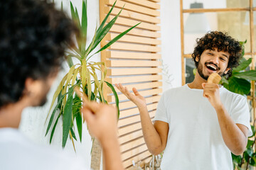 Happy playful overjoyed mixed race man singing holding a wooden comb as a microphone at modern...