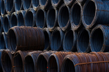 Stack of round steel wire coils at a freight station ready for transport. Metal reels for further industrial processing forming a graphic background structure with shades of grey and rusty spots.