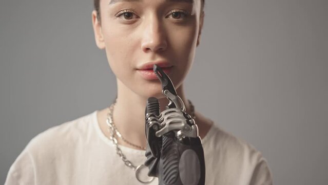 Cropped slowmo portrait of young woman with bionic arm holding finger on her lips at gray background