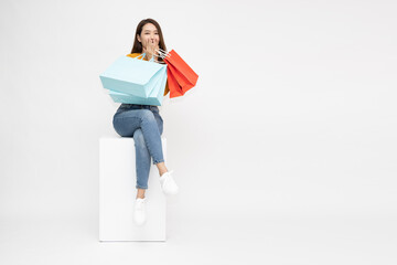 Portrait of Asian woman sitting on white box and holding shopping bags isolated on white...